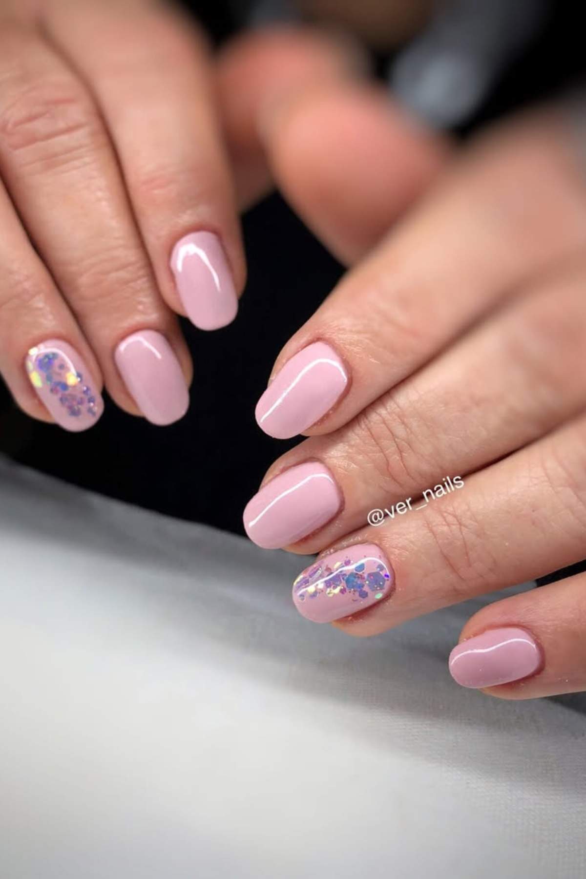 Hands with light pink manicured nails; ring fingers feature colorful floral nail art with purple and pink accents.