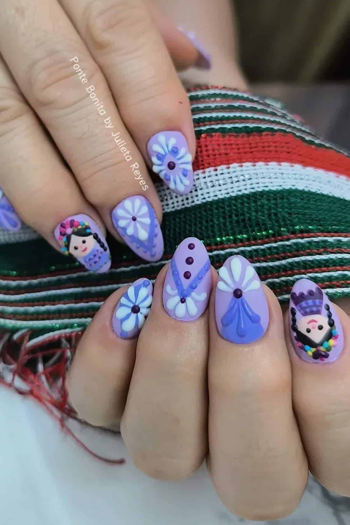 Close-up of hands with purple and white nail art featuring flowers and traditional Mexican doll designs, holding a green, white, and red woven fabric.