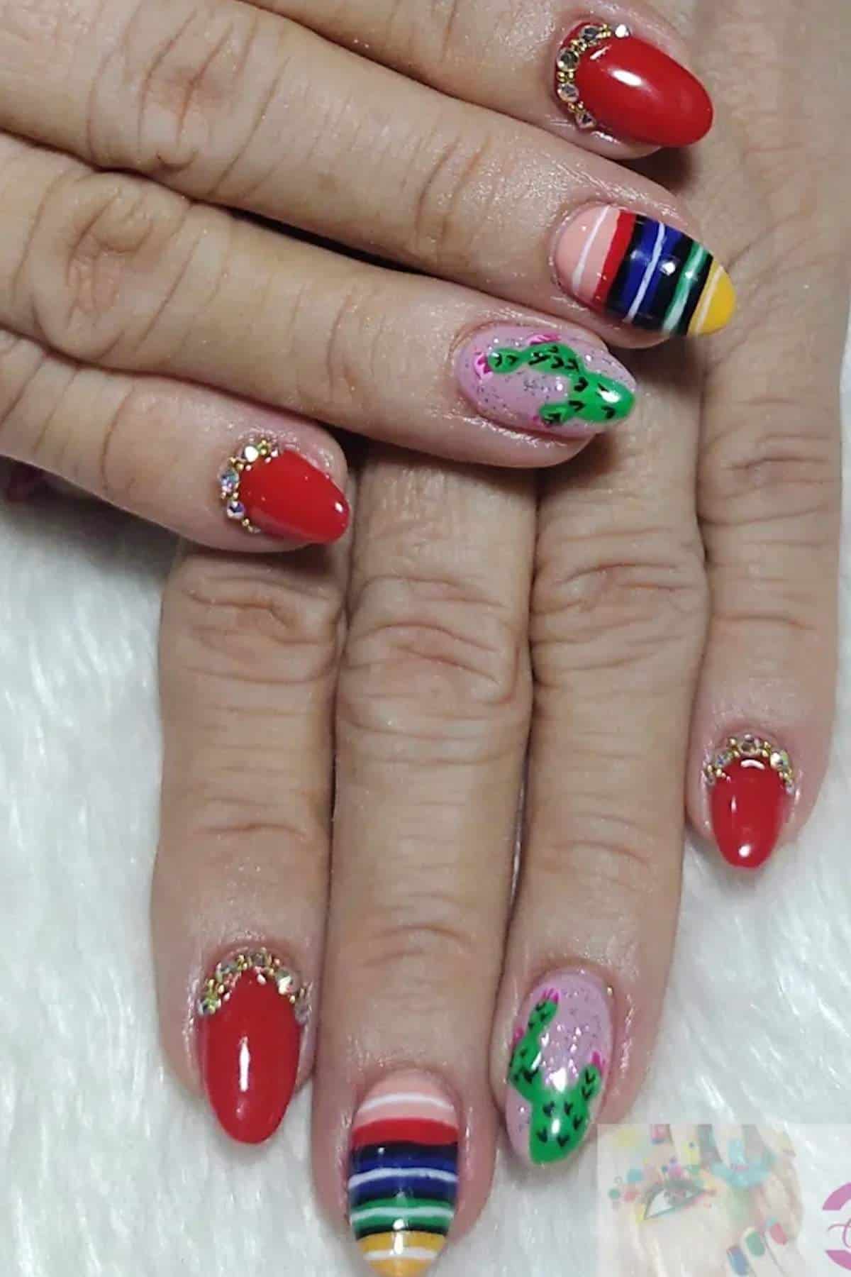 Hands with manicured nails featuring red polish, colorful horizontal stripes, gold embellishments, and cactus designs on two accent nails.