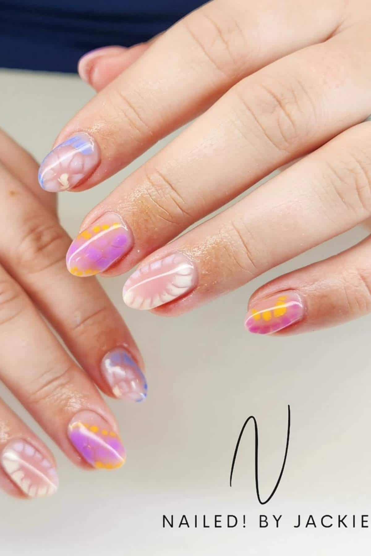 Hands with medium-length oval nails painted with colorful abstract designs in pastel shades of pink, purple, orange, blue, and white. Text reads "Nailed! By Jackie.