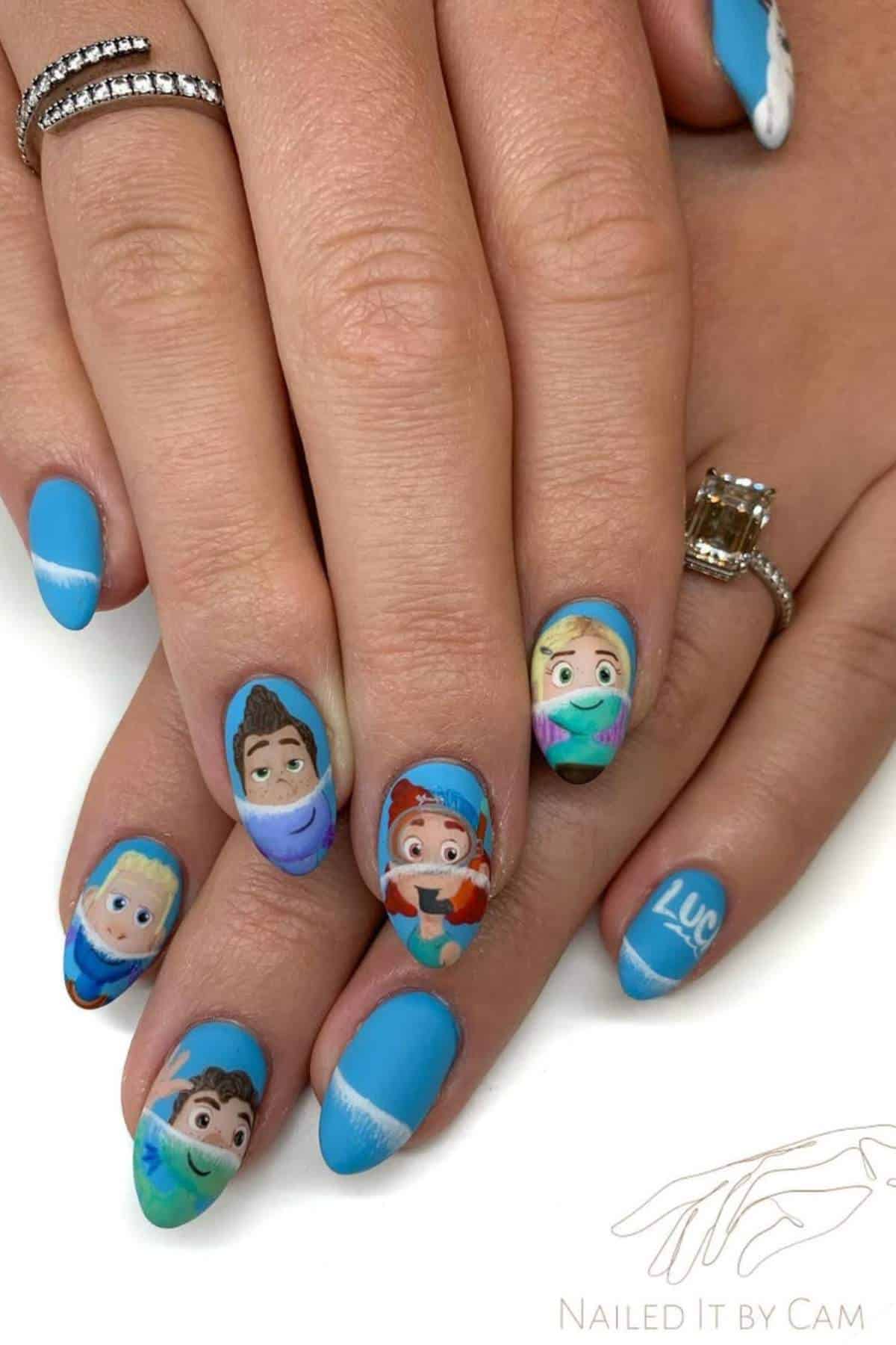 A hand with blue-themed nail art featuring detailed cartoon character faces and the word "Luca" painted on one fingernail.