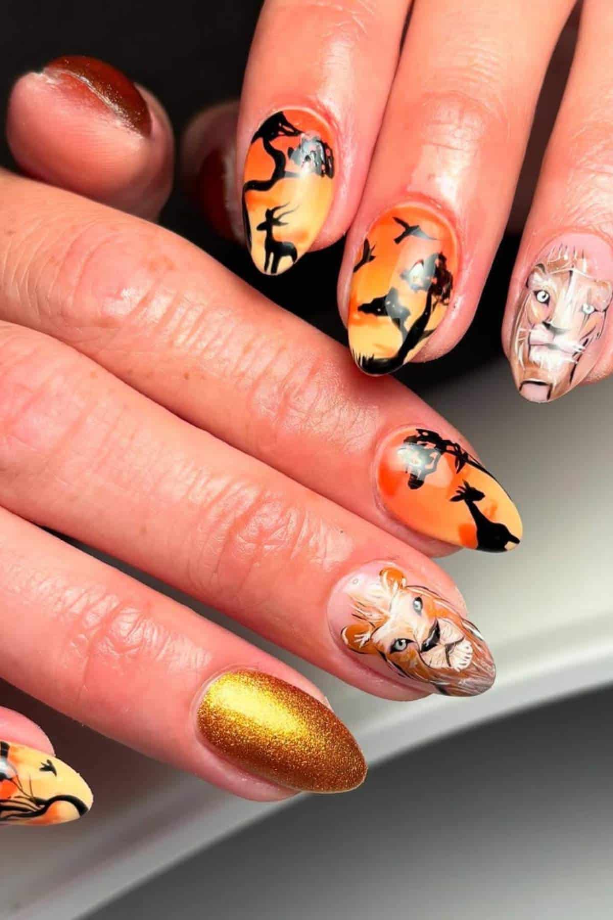 A hand with long nails featuring safari-themed nail art, including silhouettes of animals, a lion's face, and one metallic gold nail.