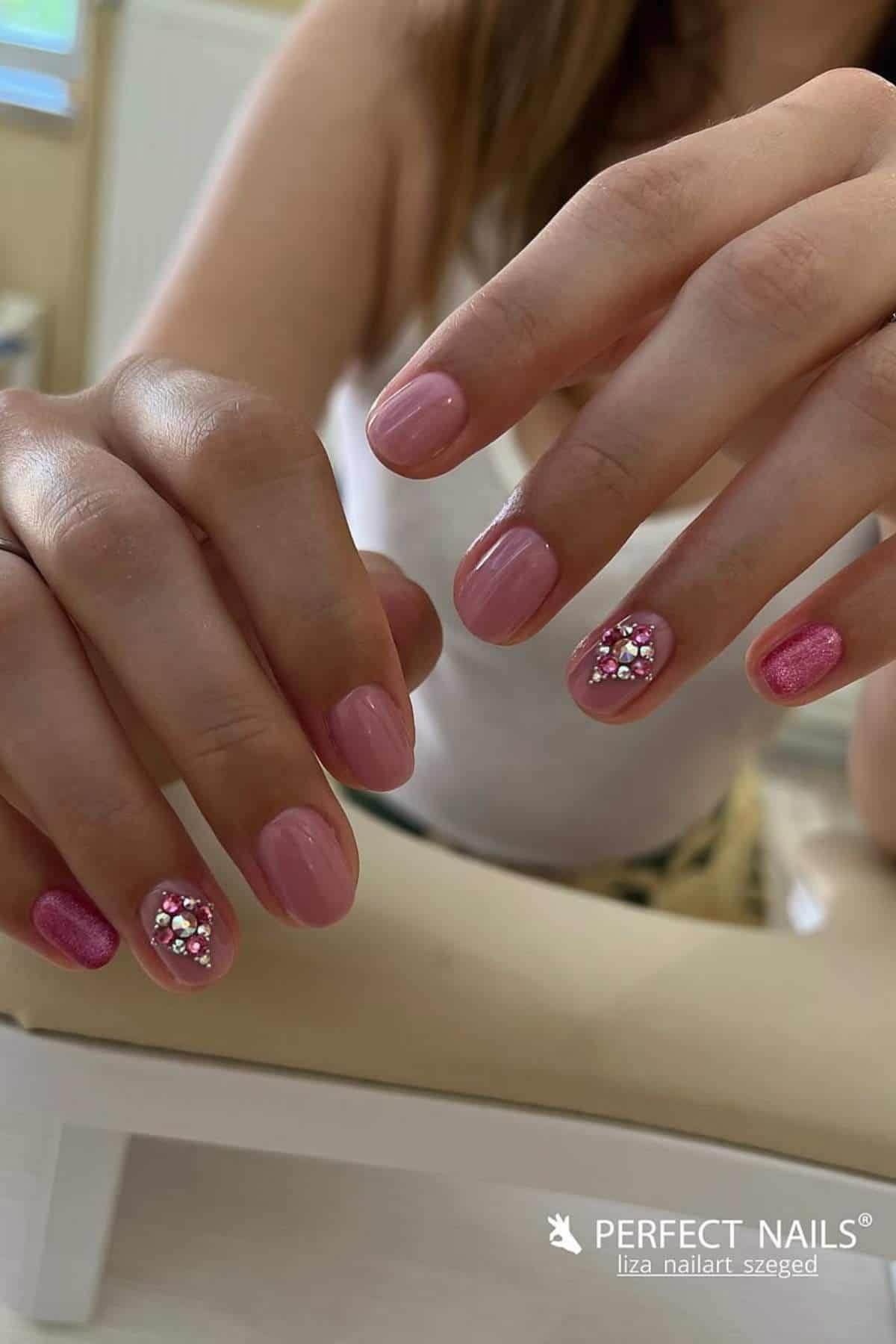 Hands with short, rounded pink nails; ring fingers are decorated with rhinestones and glitter. Person is wearing a sleeveless top. "PERFECT NAILS" logo is visible in the corner.