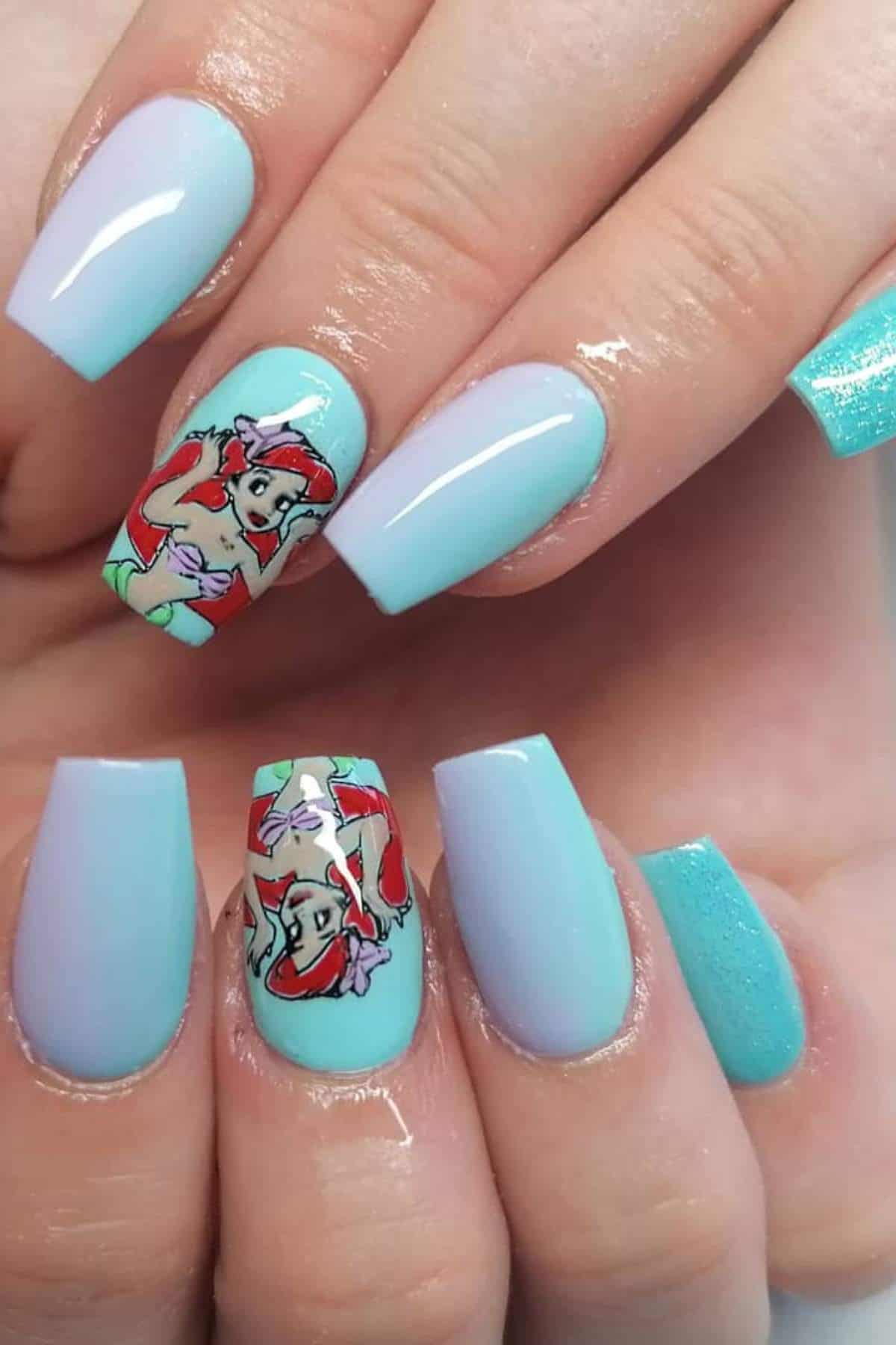 A hand with pastel blue and purple gradient nails, featuring cartoon designs of Ariel from The Little Mermaid on the middle and ring fingernails.