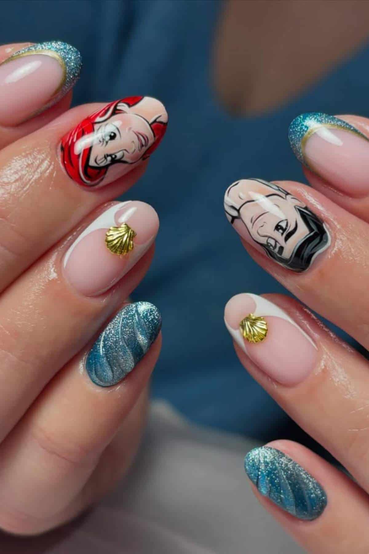 Hands with manicured nails featuring blue glitter tips, gold shell charms, and cartoon character faces painted on two nails.