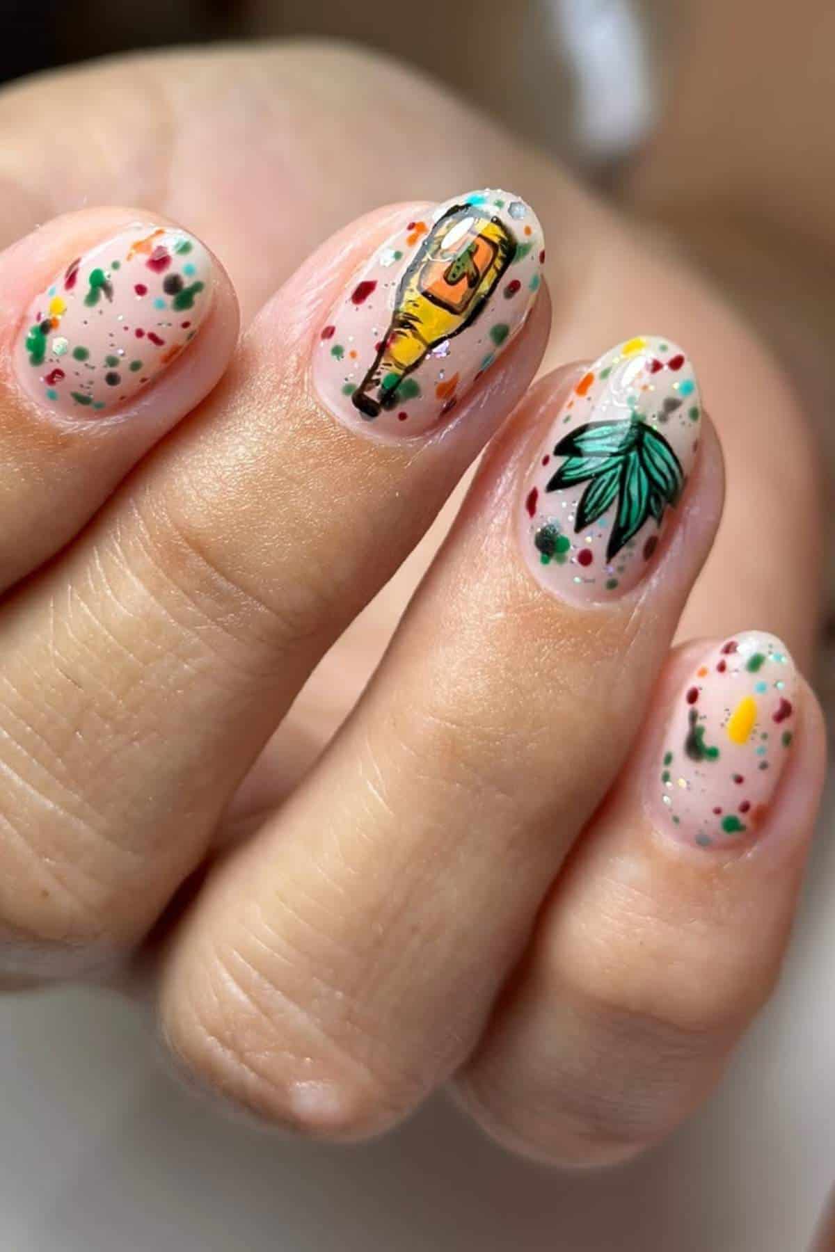 A hand with oval nails featuring colorful speckles and detailed nail art, including a taco and a green leafy design on a nude base.