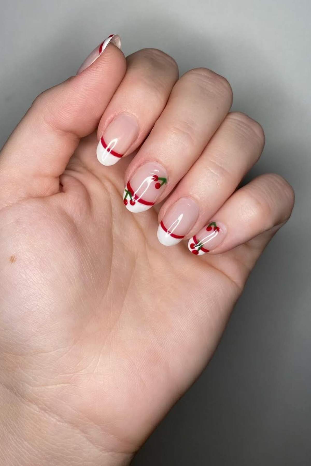A hand with manicured nails featuring French tips and small cherry designs on a light background.