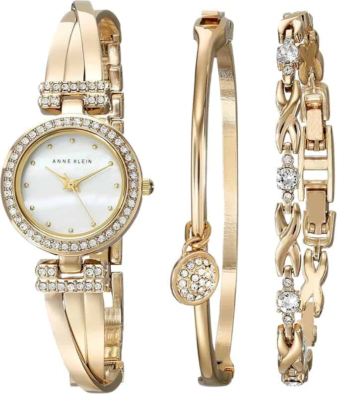 A gold Anne Klein women's watch with a crystal-studded bezel and matching gold bracelets, one with crystals and one with a round crystal charm, displayed side by side.