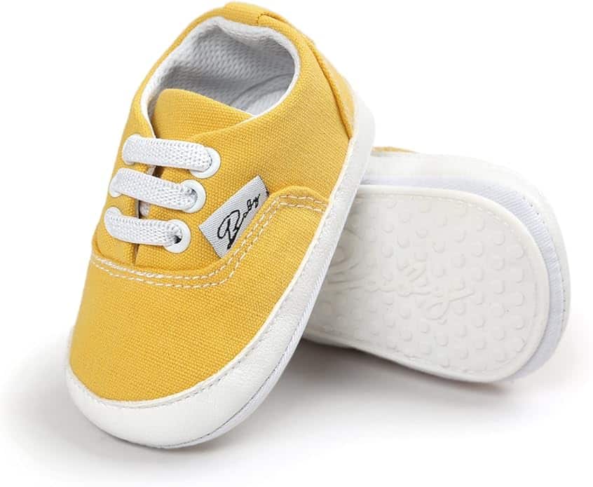 A pair of yellow baby shoes with white soles and white laces, one shoe standing upright and the other lying on its side.