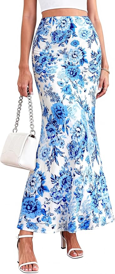 A woman wearing a long, high-waisted white skirt with a blue floral pattern, white sandals, a white crop top, and holding a white handbag.