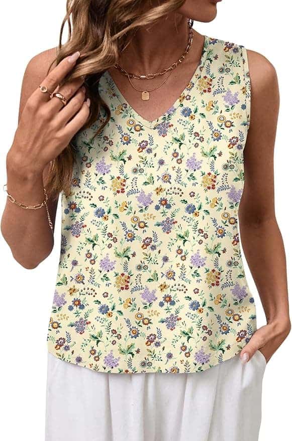 Woman wearing a sleeveless, V-neck top with a multicolored small floral pattern and white pants. She has wavy hair and is accessorized with gold jewelry.