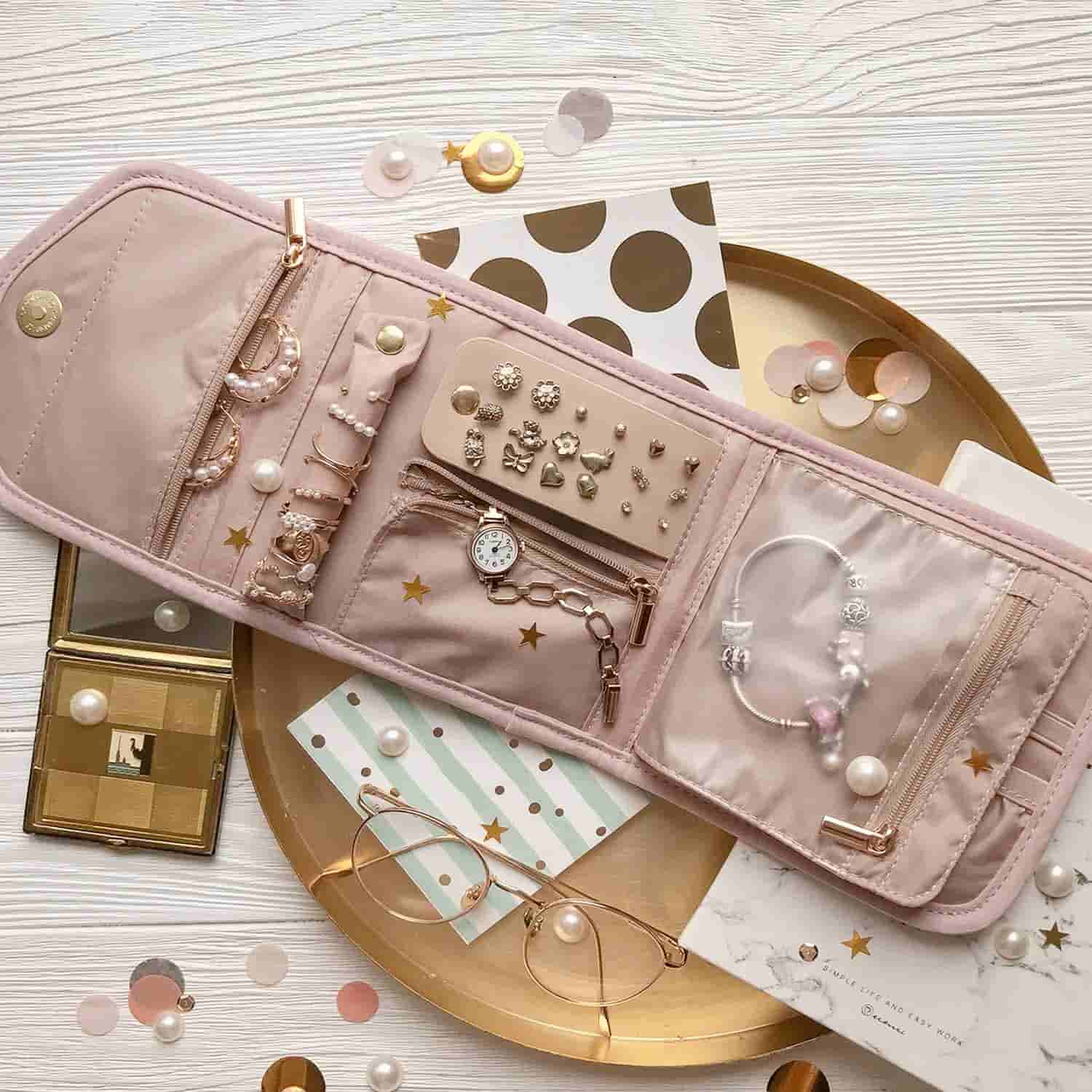 A pink jewelry organizer displaying earrings, rings, a watch, and bracelets is laid open on a white surface with scattered accessories and decorative items.