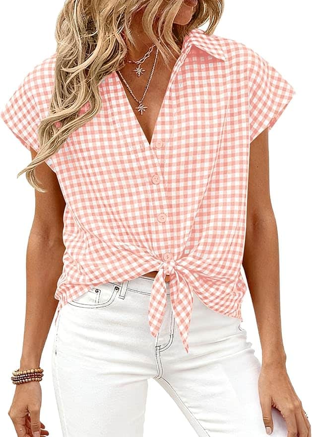 Woman wearing a short-sleeve, pink and white gingham button-down shirt tied at the waist, paired with white jeans and layered necklaces.