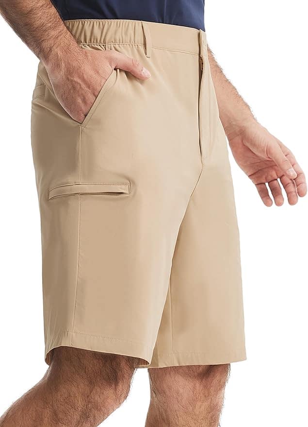 A man wearing beige knee-length shorts with side and back pockets, standing with one hand in his pocket.