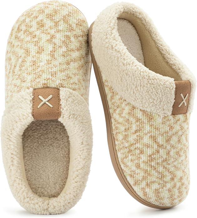A pair of cream and beige patterned slippers with plush lining and brown accents, featuring an "X" stitch detail on the front.