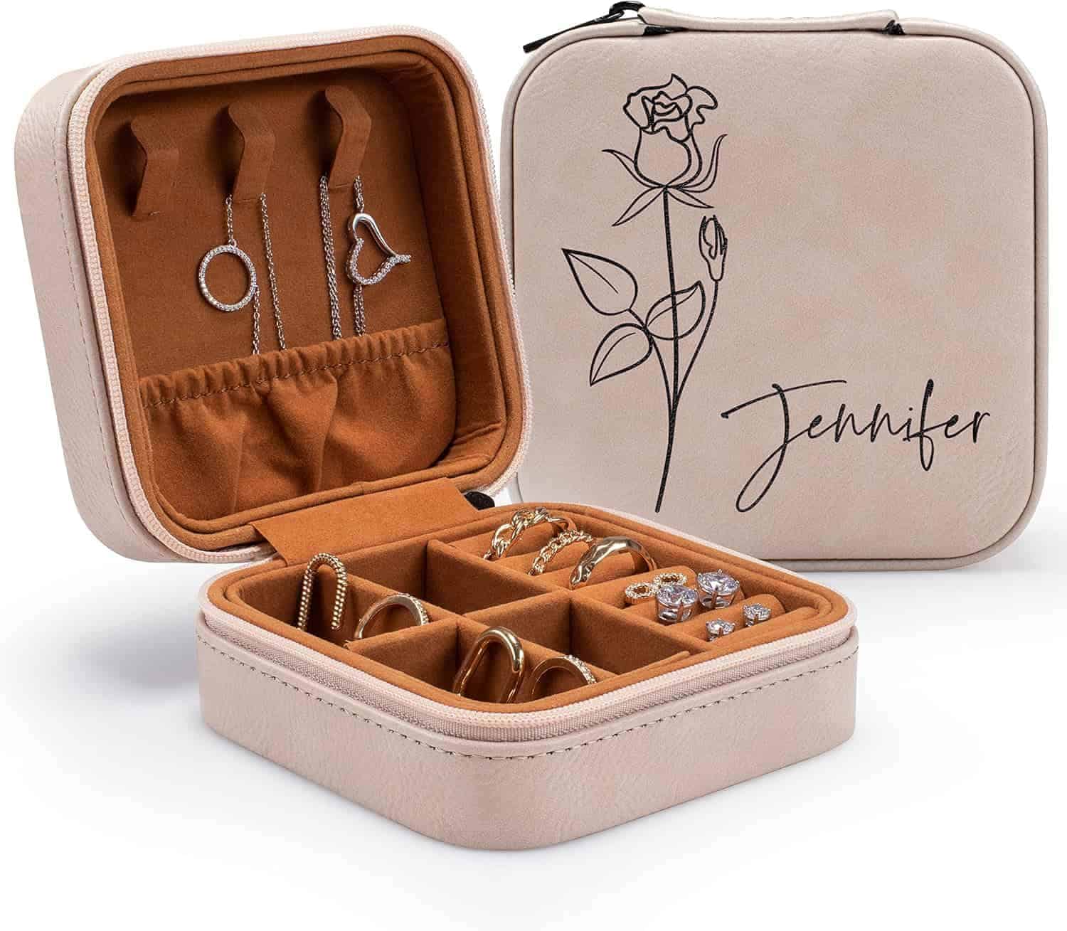 Beige jewelry box with compartments, holding earrings, rings, and bracelets. The lid is decorated with a rose illustration and the name “Jennifer.”.