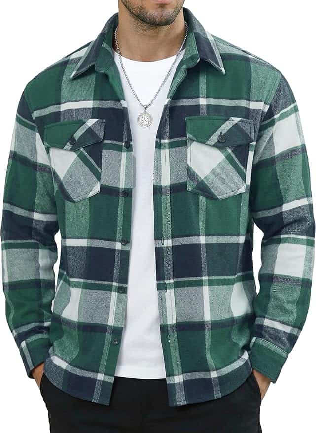 A man wearing a green, white, and navy plaid flannel shirt over a white t-shirt, with black pants and a silver necklace.