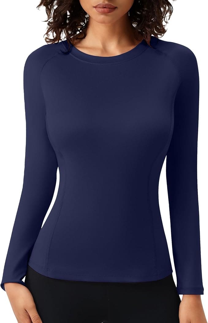 A woman wearing a fitted, long-sleeve, navy blue athletic top with black pants, shown from the waist up.