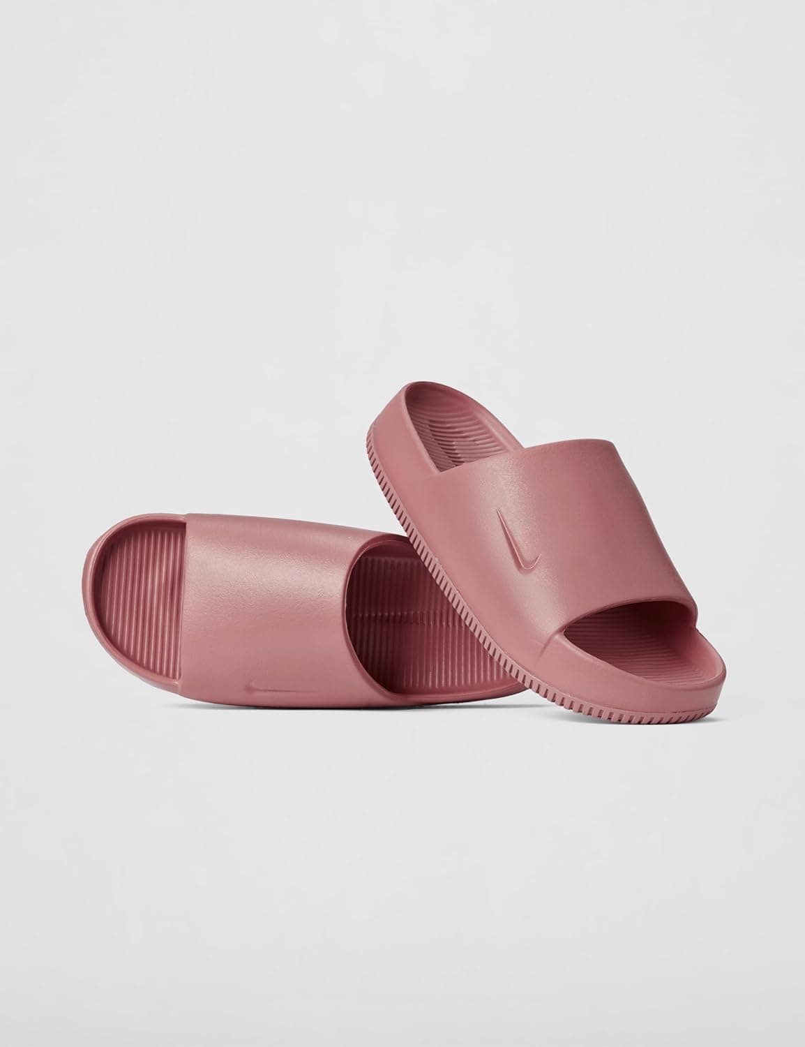 A pair of pink slide sandals with a minimalist design, featuring a single wide strap and subtle groove detailing on the footbed and sole.