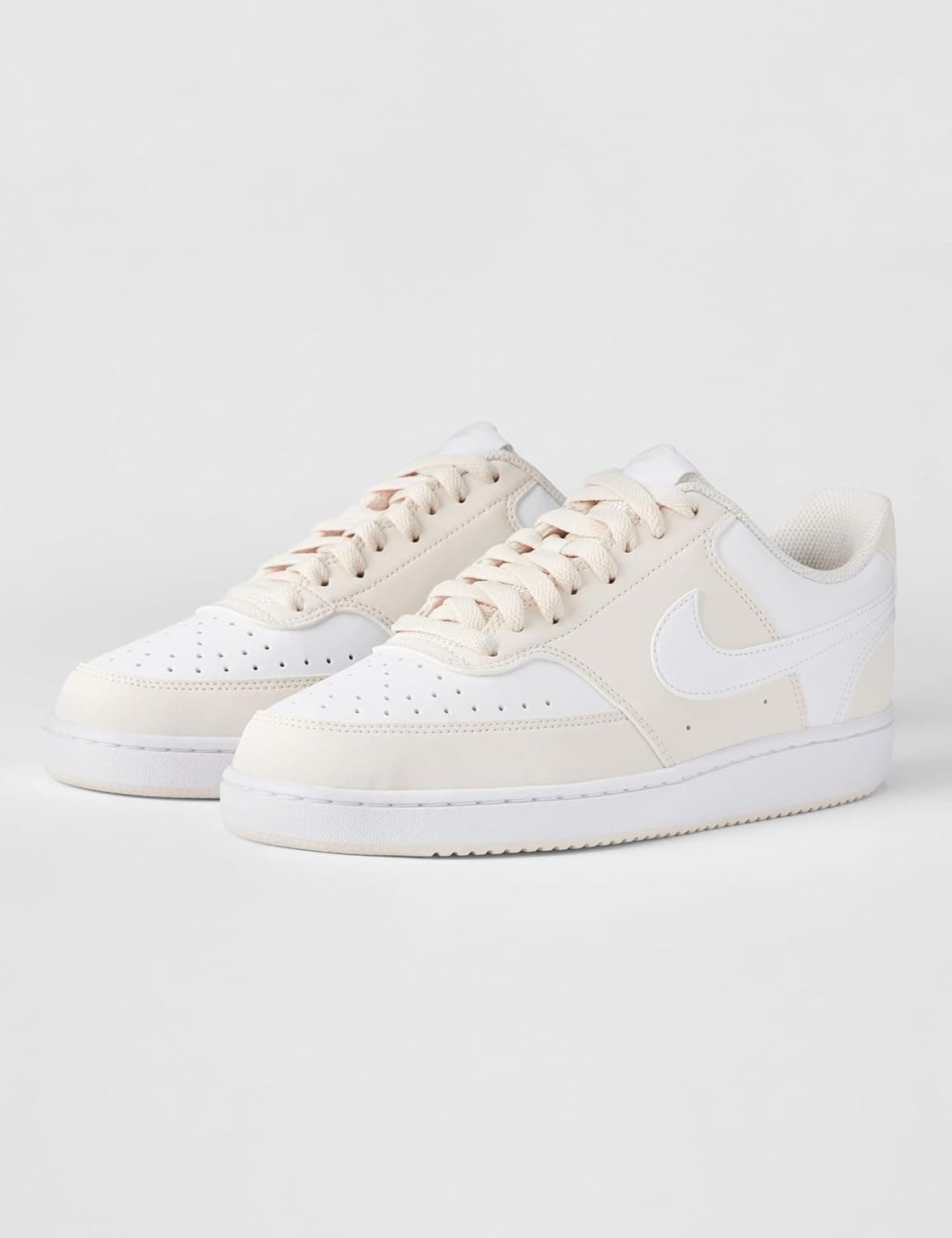 A pair of low-top beige and white Nike sneakers with white soles and laces, displayed on a plain light background.