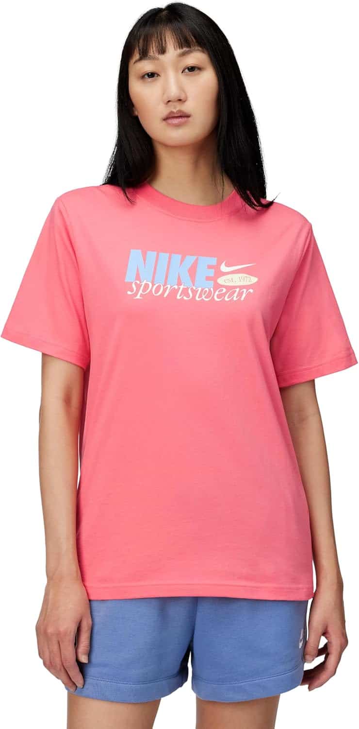 Woman wearing a pink Nike Sportswear T-shirt and blue shorts, standing against a plain white background.