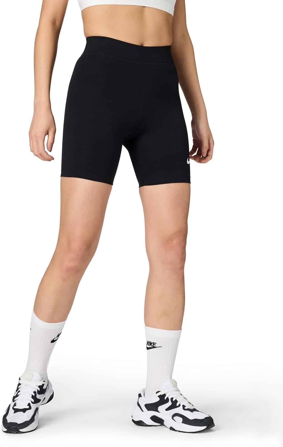 Person wearing a white crop top, black high-waisted biker shorts, white Nike crew socks, and white and black Nike sneakers, standing against a plain background.