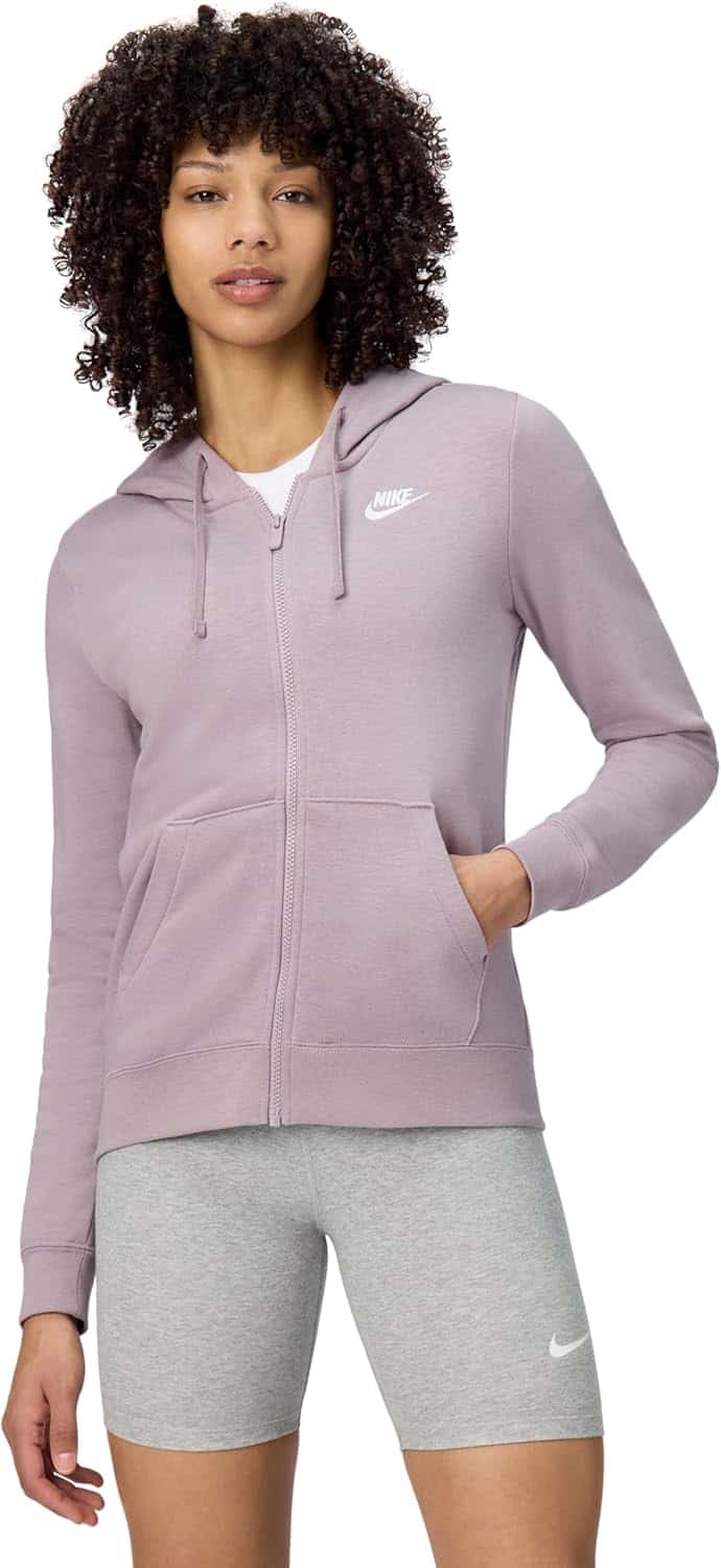 A person wearing a light purple Nike zip-up hoodie and light gray Nike shorts, standing with one hand in their pocket against a plain background.