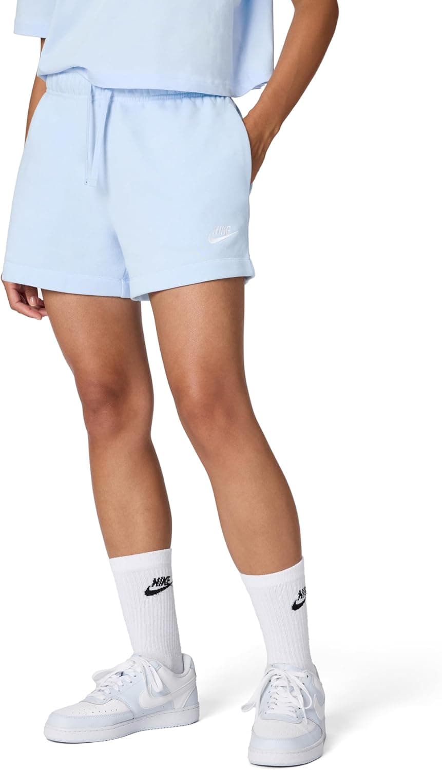 Person wearing light blue Nike shorts, matching top, white Nike sneakers, and white Nike socks, standing with one hand in shorts pocket against a white background.