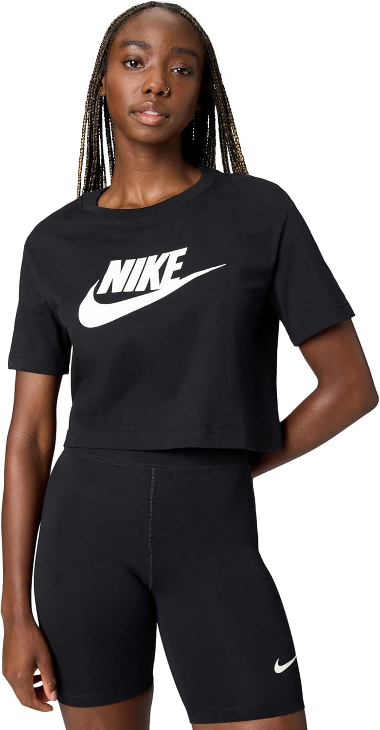 A woman wearing a black Nike cropped t-shirt and black Nike biker shorts stands with one hand on her hip against a white background.