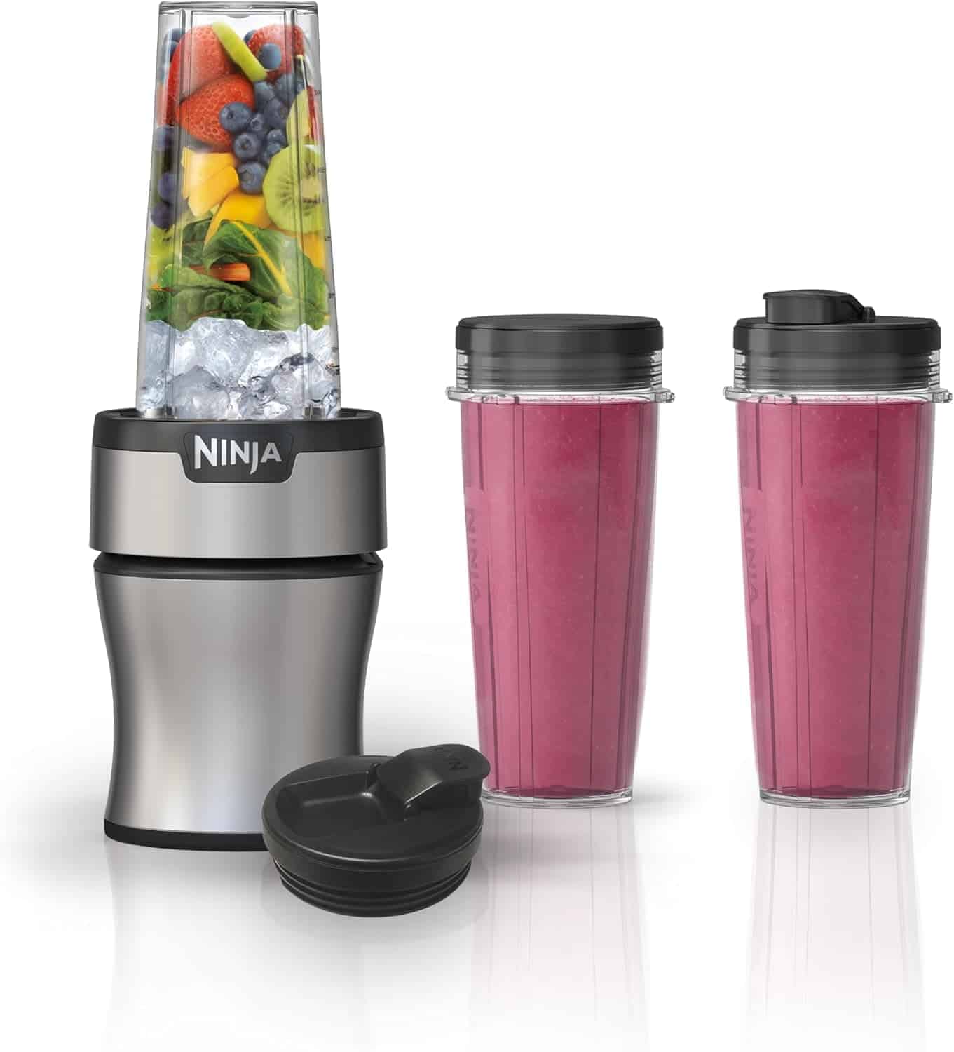 A Ninja blender with a blending cup filled with fruit and ice, two cups with pink smoothies, and a black lid displayed on a white background.