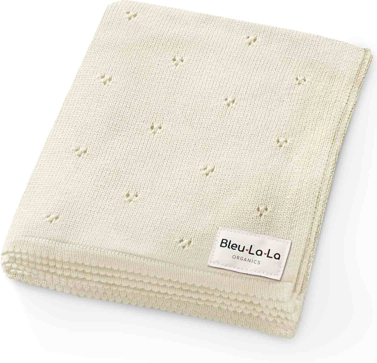 A folded, cream-colored knit blanket with small dot patterns and a "Bleu La La Organics" label in the corner.