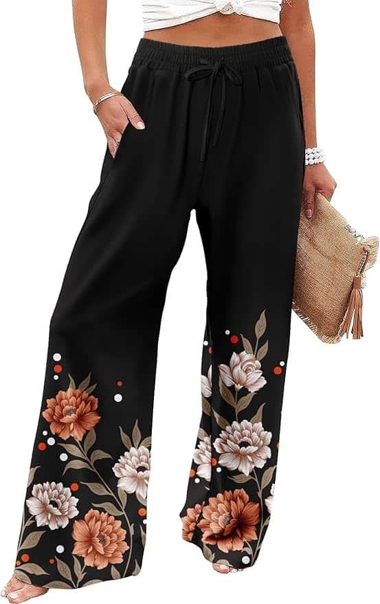 A woman wearing black wide-leg pants with a drawstring waist, floral print near the hems, and holding a woven clutch bag.
