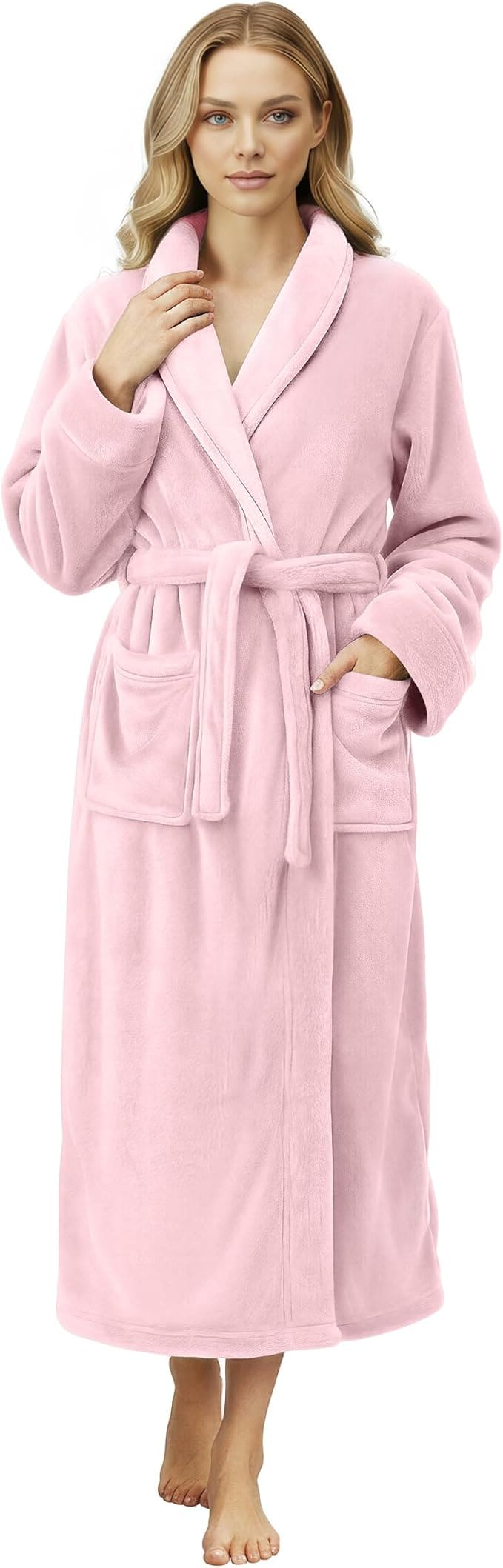 Woman wearing a long, light pink bathrobe with a belt and two front pockets, standing barefoot against a plain background.