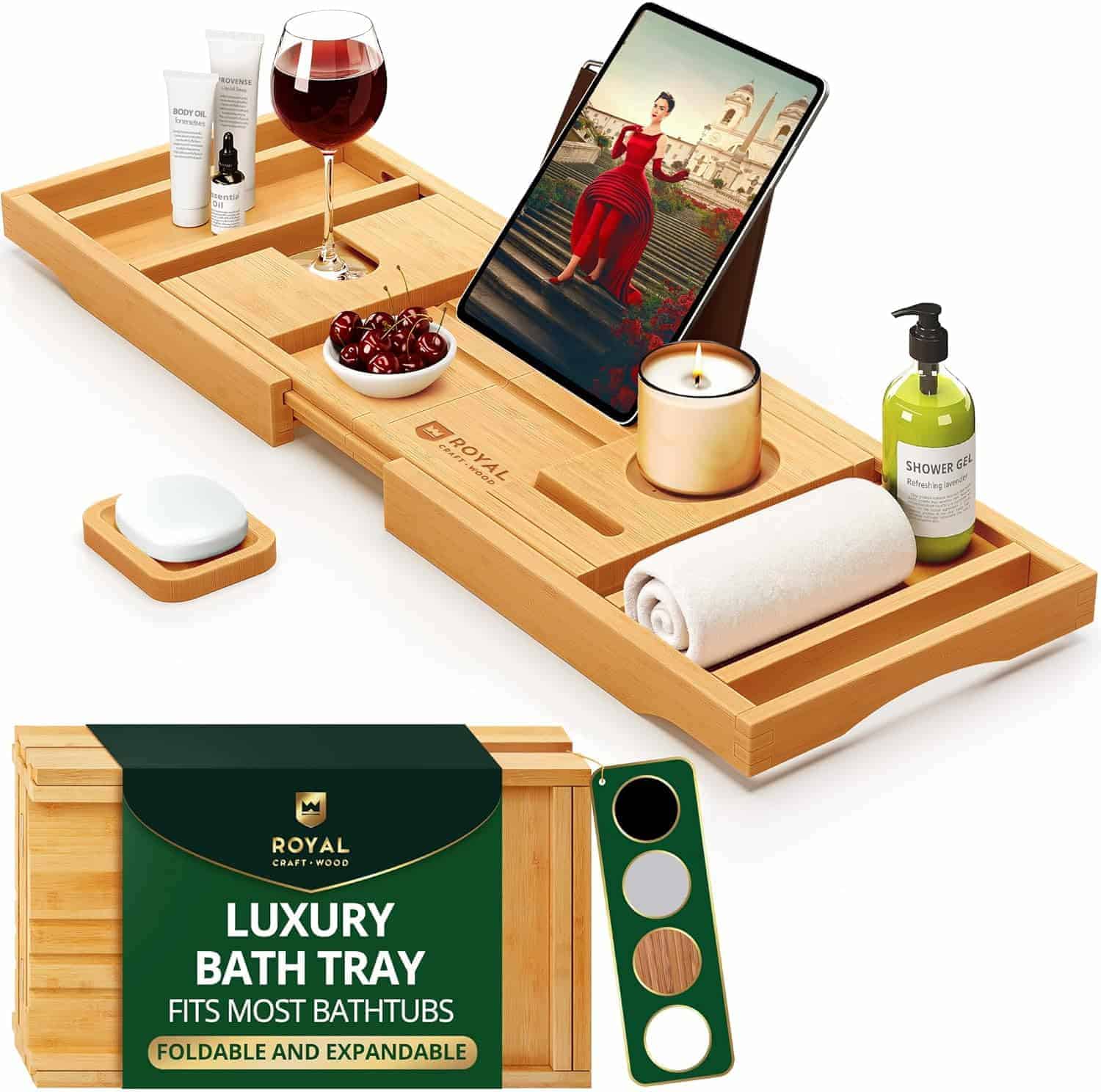 A wooden bath tray holds a tablet, wine glass, candle, towel, soap, lotion, berries, and toiletries. Packaging in the foreground reads "Luxury Bath Tray.