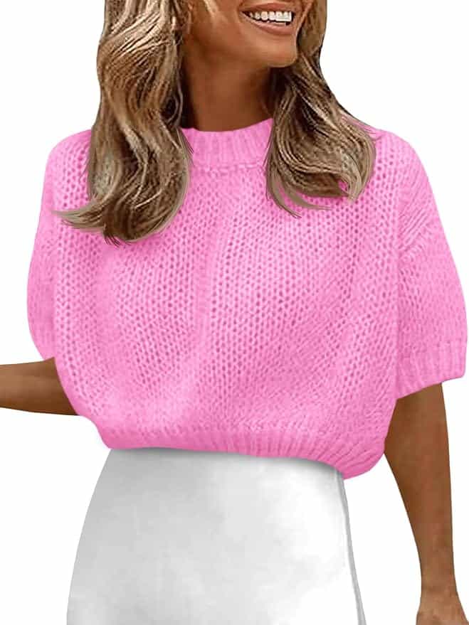 A woman wearing a bright pink short-sleeve knit sweater and a white high-waisted skirt, smiling and facing slightly to the side.