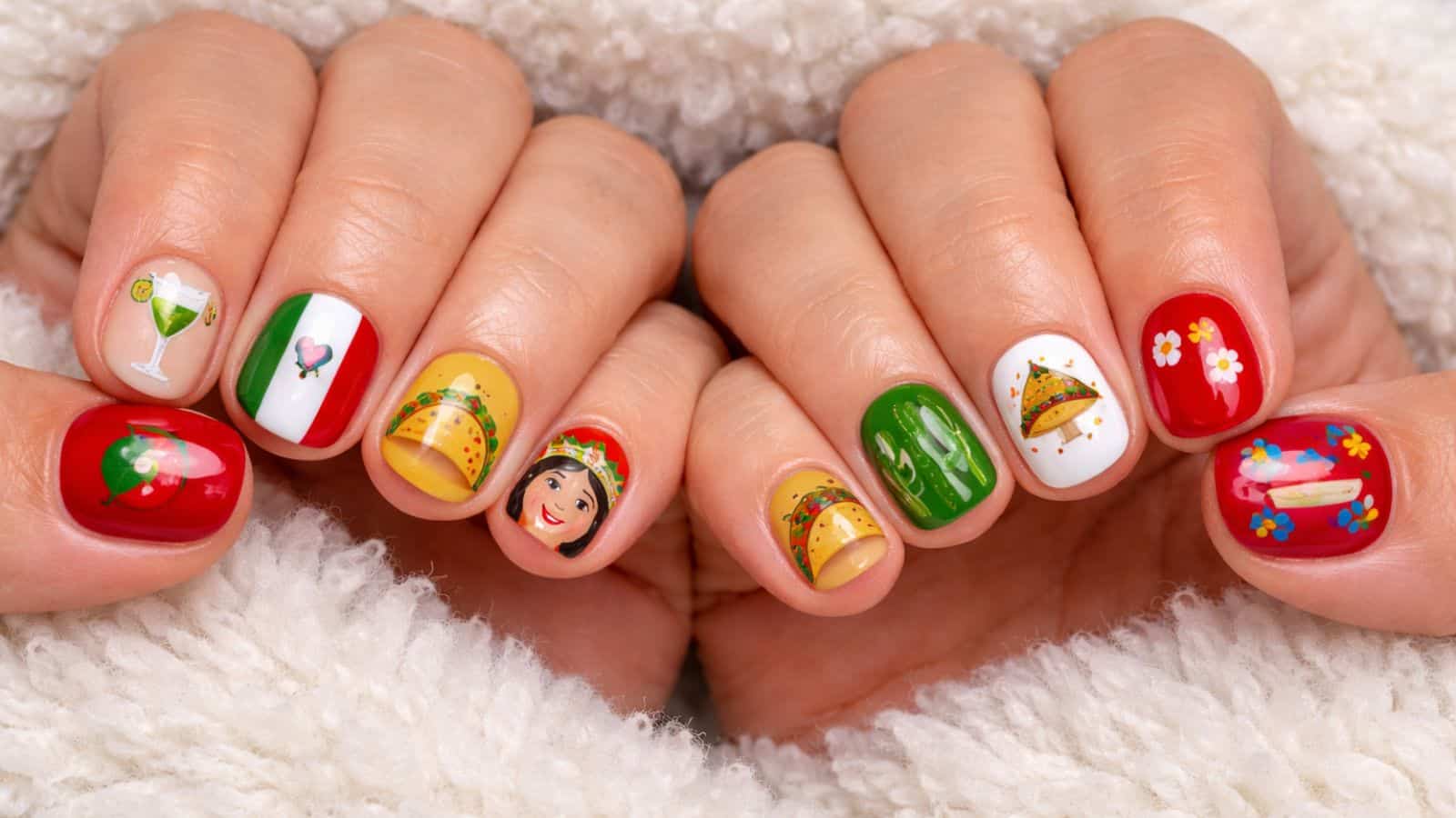 Hands with colorful nail art featuring tacos, margaritas, the Mexican flag, cactus, flowers, and a Frida Kahlo's face, set against a white fluffy background.