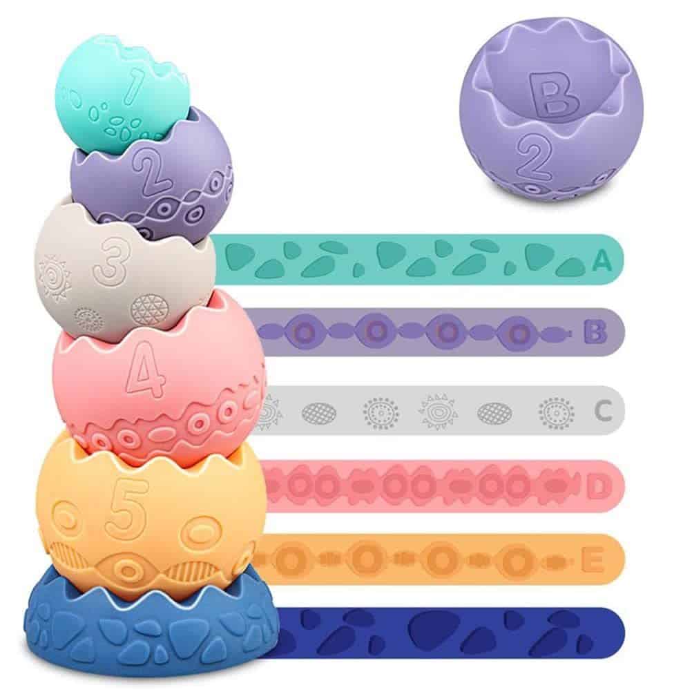 Stackable toy set with five colorful, textured, numbered egg-shaped cups and matching flat strips in various colors. One ball is shown separately at the top right.