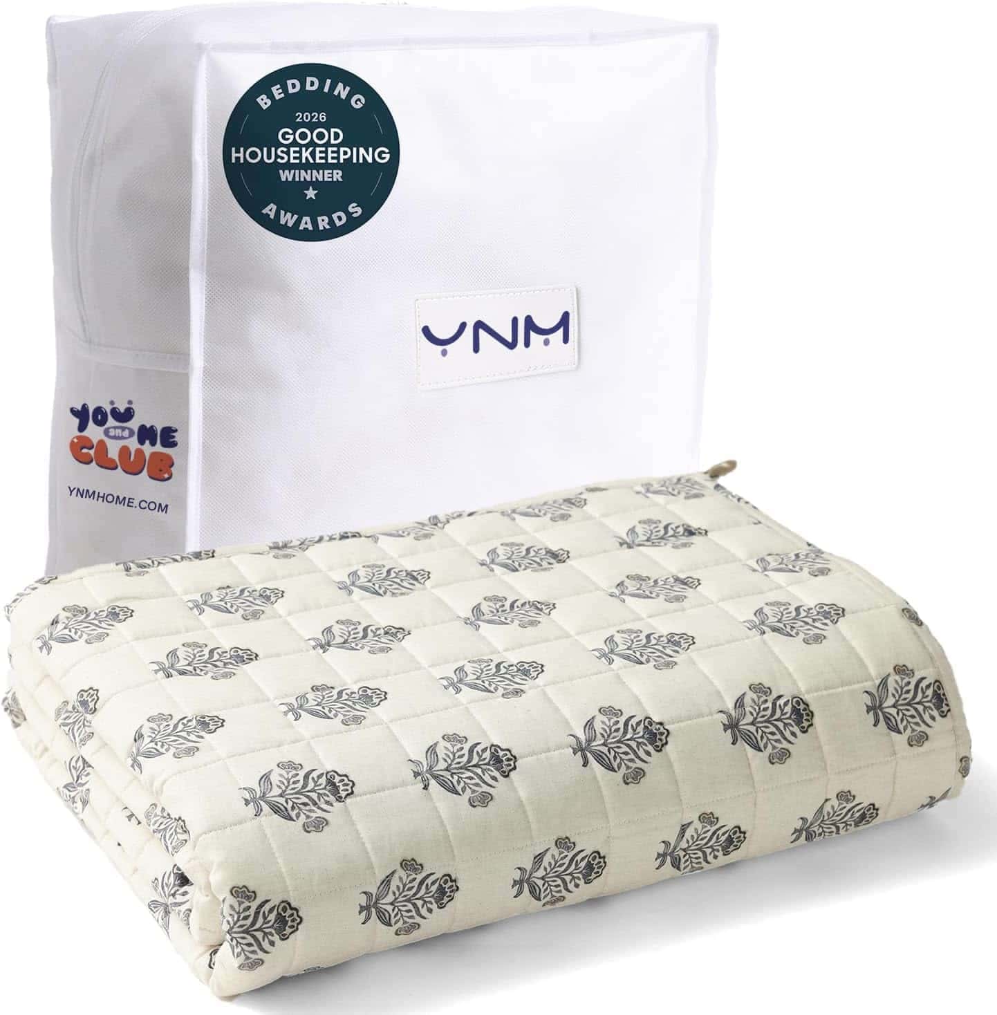 A folded patterned blanket is displayed in front of a white storage bag labeled “YNM” with a “Bedding Awards” sticker on it.