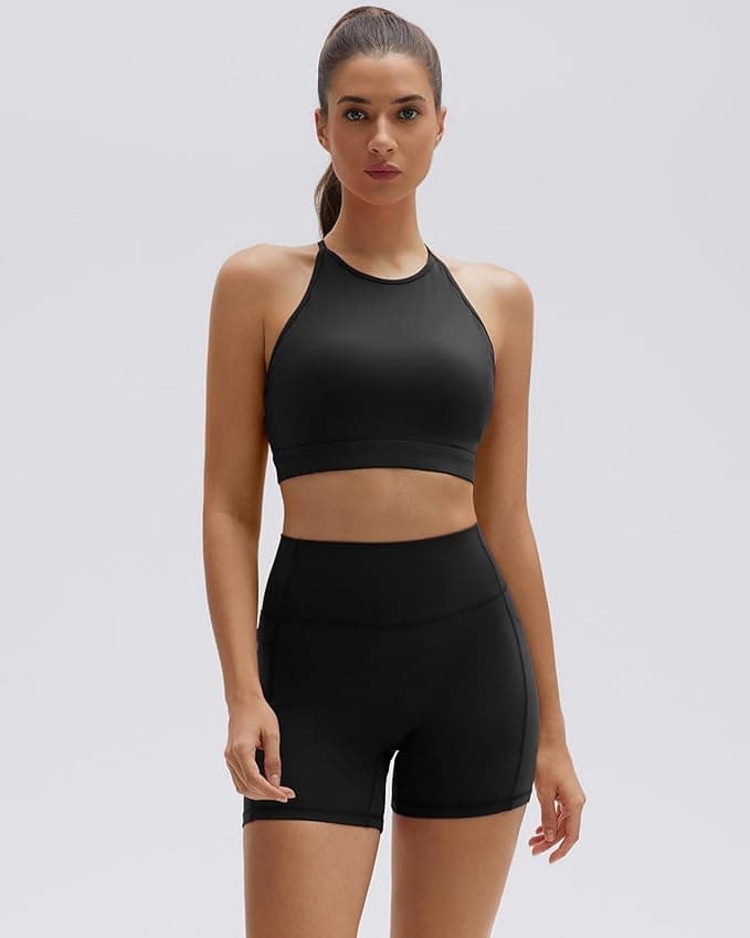 A woman stands facing forward wearing a black sports bra and matching high-waisted athletic shorts against a plain light background.