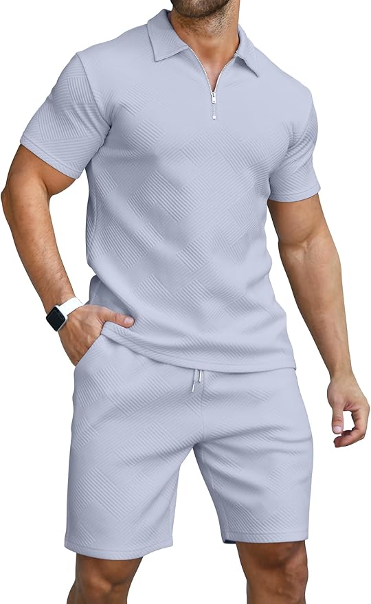 A man wearing a light grey short-sleeve zip-up shirt and matching shorts with a subtle textured pattern, standing with one hand in his pocket.