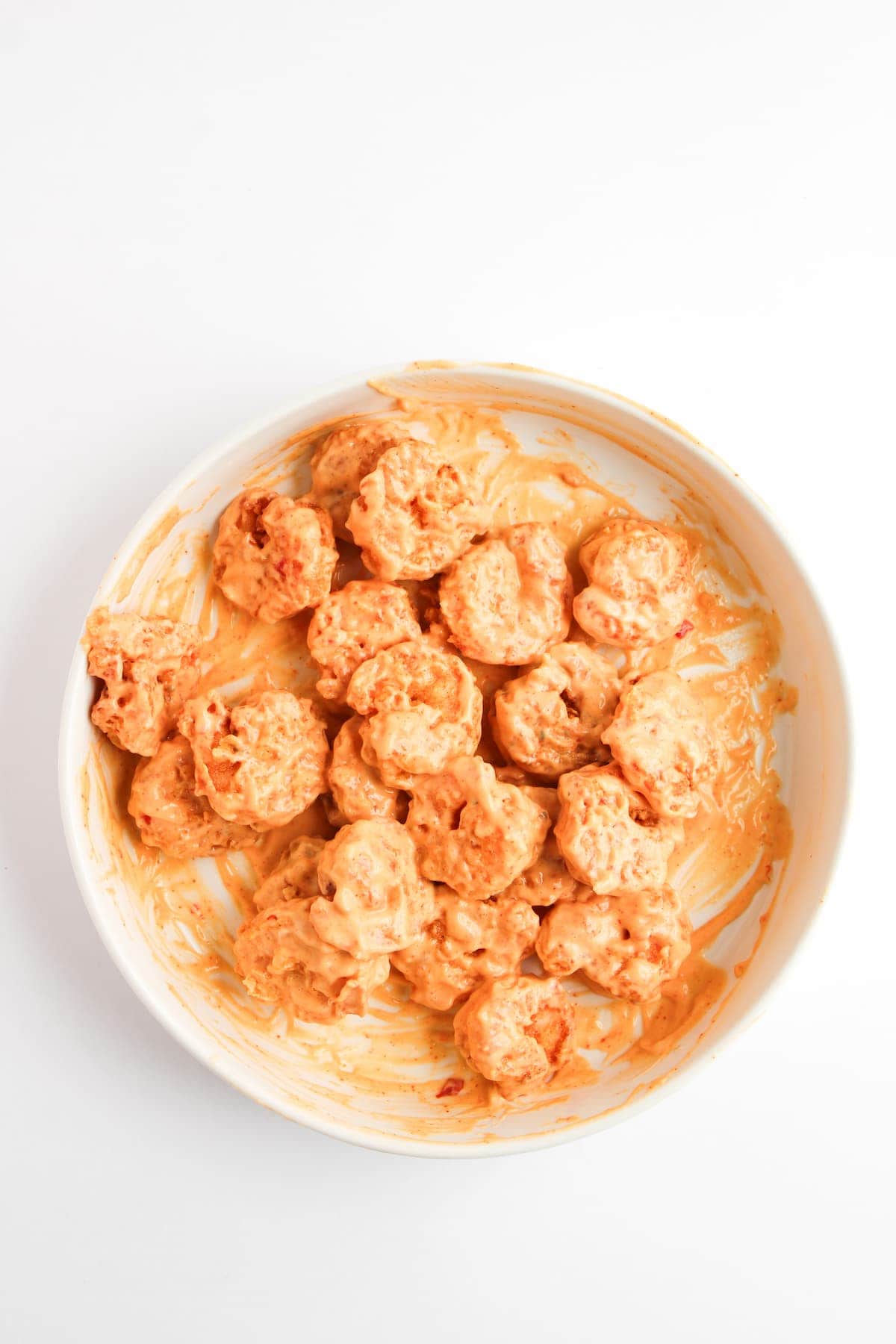 A white bowl filled with coated shrimp in an orange creamy sauce, placed on a plain white background.