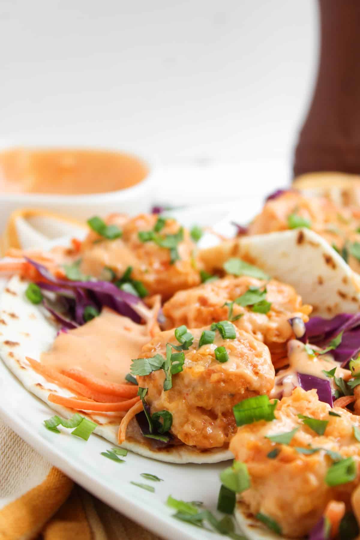 A close-up of tacos filled with saucy meatballs, shredded carrots, purple cabbage, and topped with chopped green onions on a white plate.