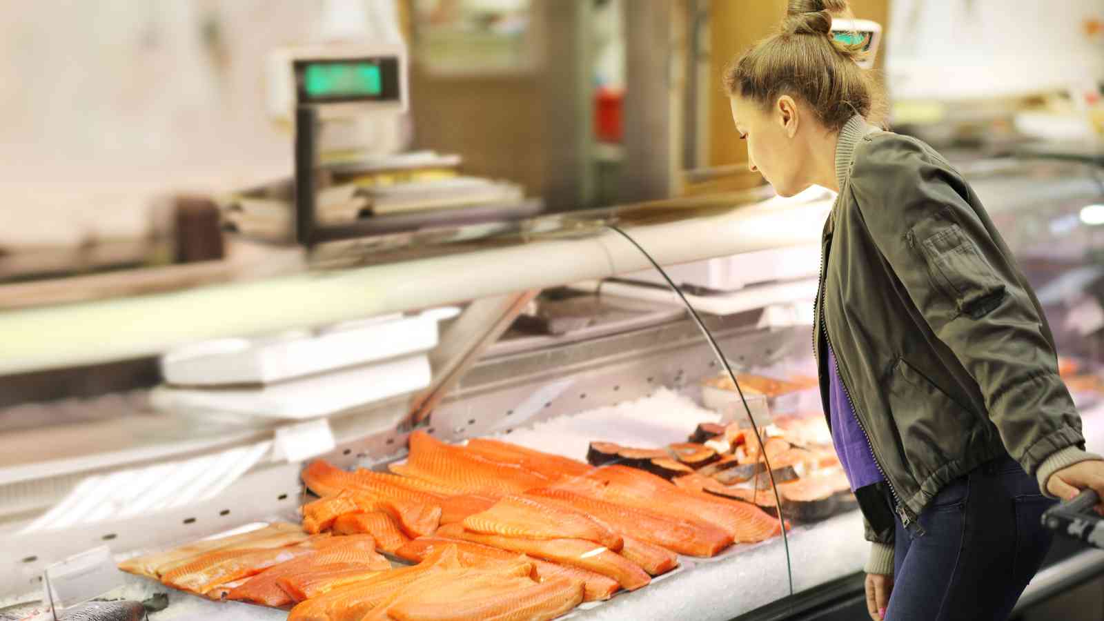 A woman examines fresh salmon fillets displayed on ice at a seafood counter in a grocery store.