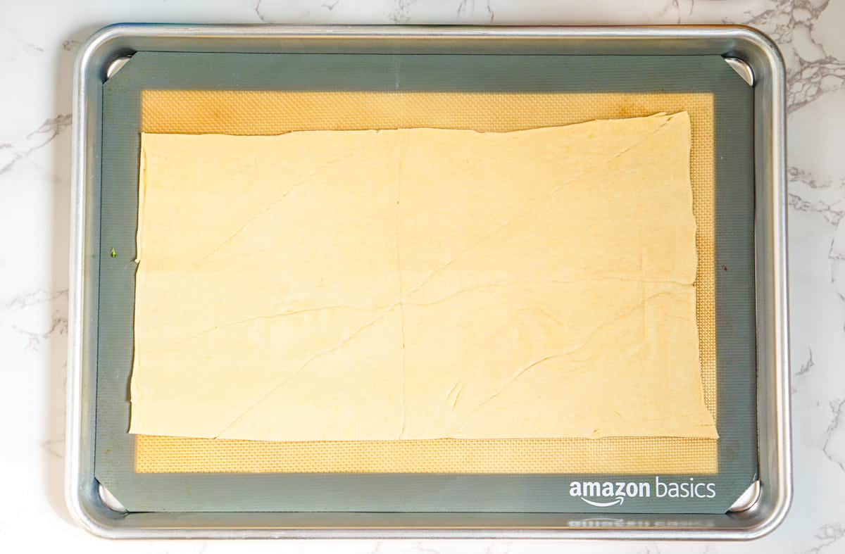 A rectangular sheet of raw dough is placed on a silicone baking mat on a metal baking sheet.