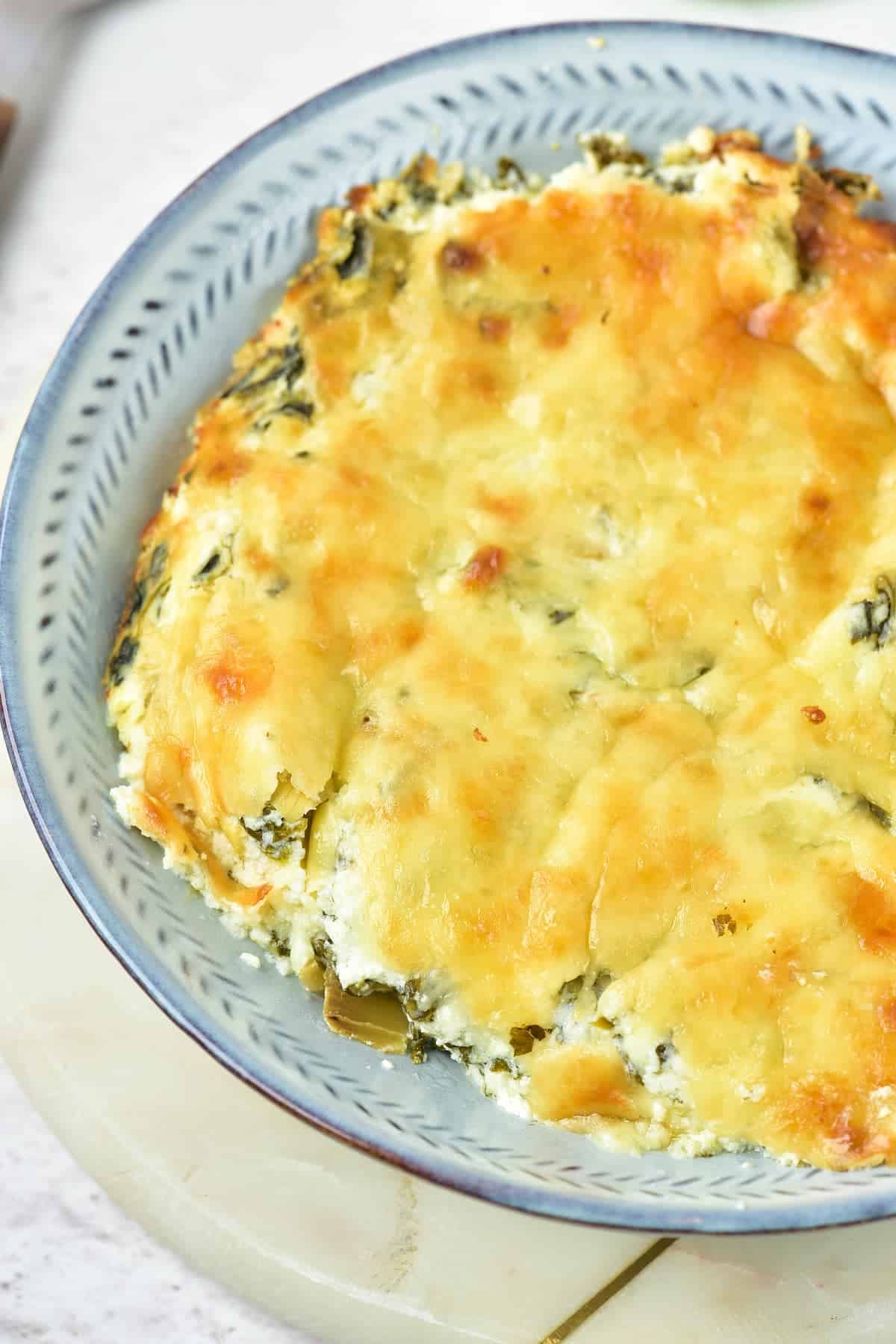 A baked spinach and cheese casserole in a blue patterned dish, with a golden, slightly browned top.