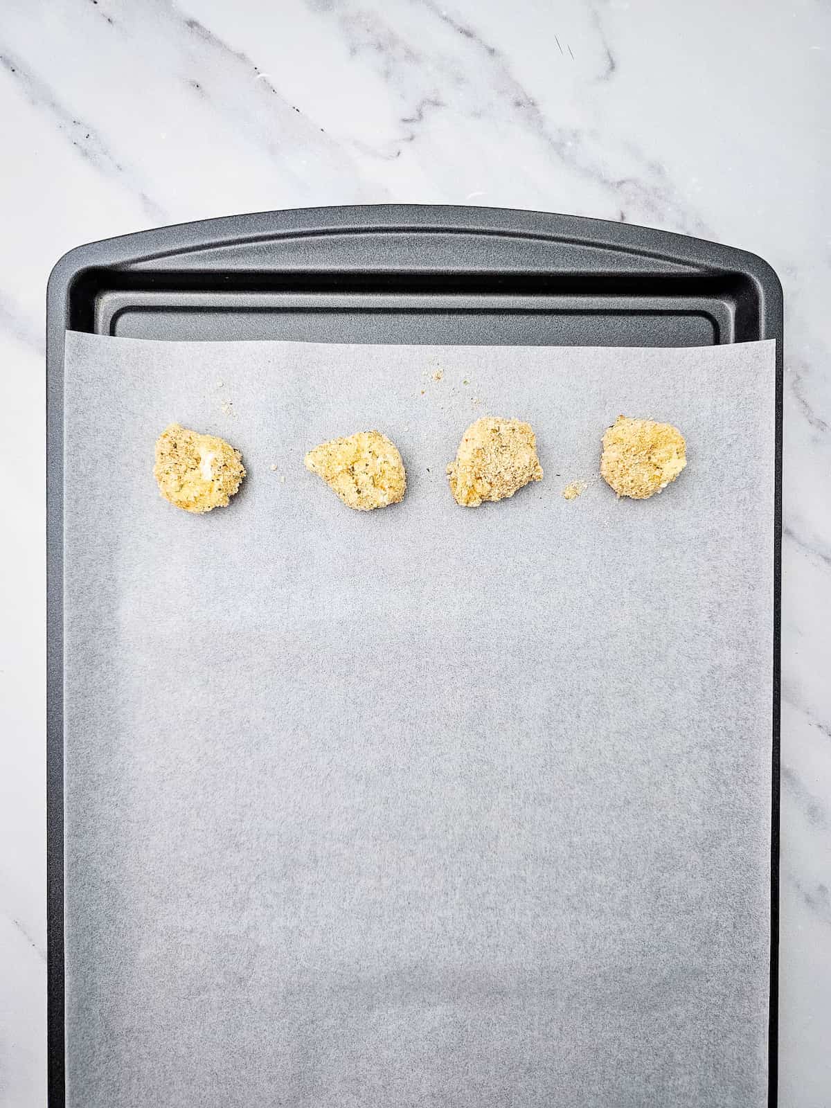 A baking sheet lined with parchment paper holds four evenly spaced balls of cookie dough near the top edge.