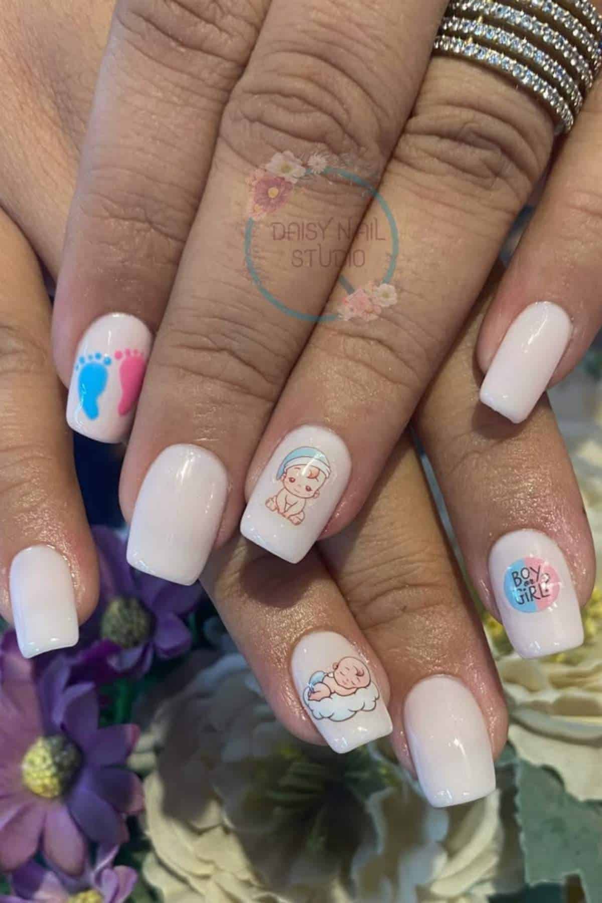 A hand with light pink manicured nails featuring baby-themed designs: blue and pink footprints, a swaddled baby, a baby on a cloud, and the words "Boy or Girl?.
