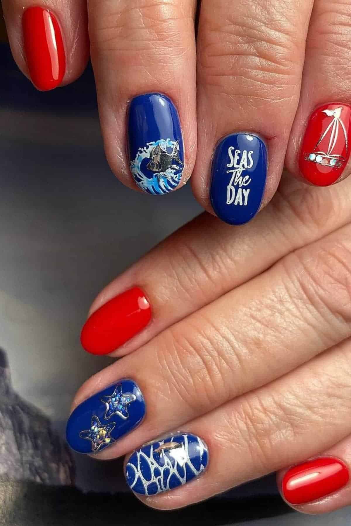 Nails painted red and blue with nautical-themed art, including a boat, waves, starfish, and the phrase "SEAS the DAY" on one nail.