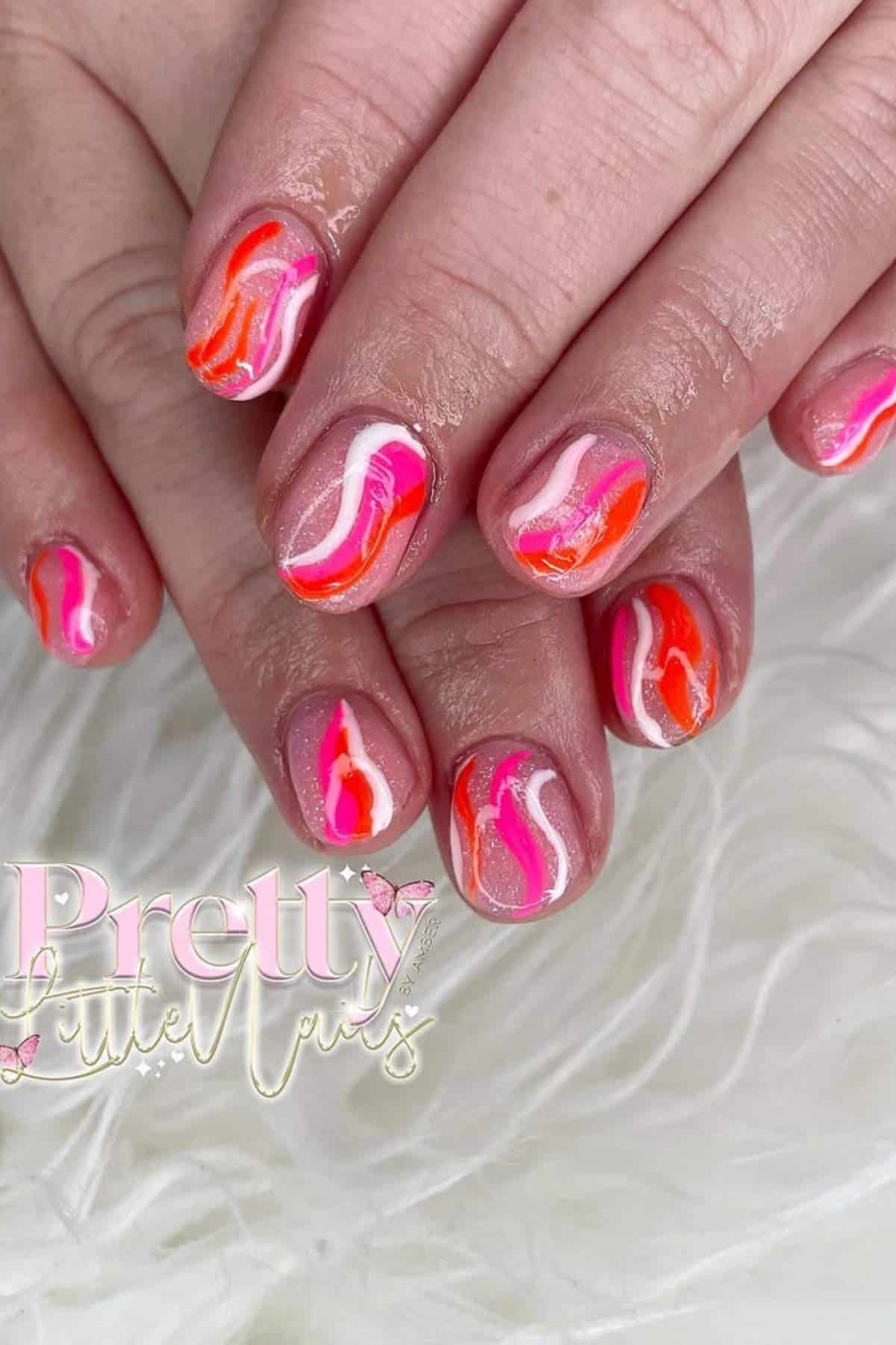 Hands with short nails featuring a pink, white, and orange wavy abstract nail art design, displayed on a white textured surface. "Pretty Little Nails" logo is visible in the lower left.