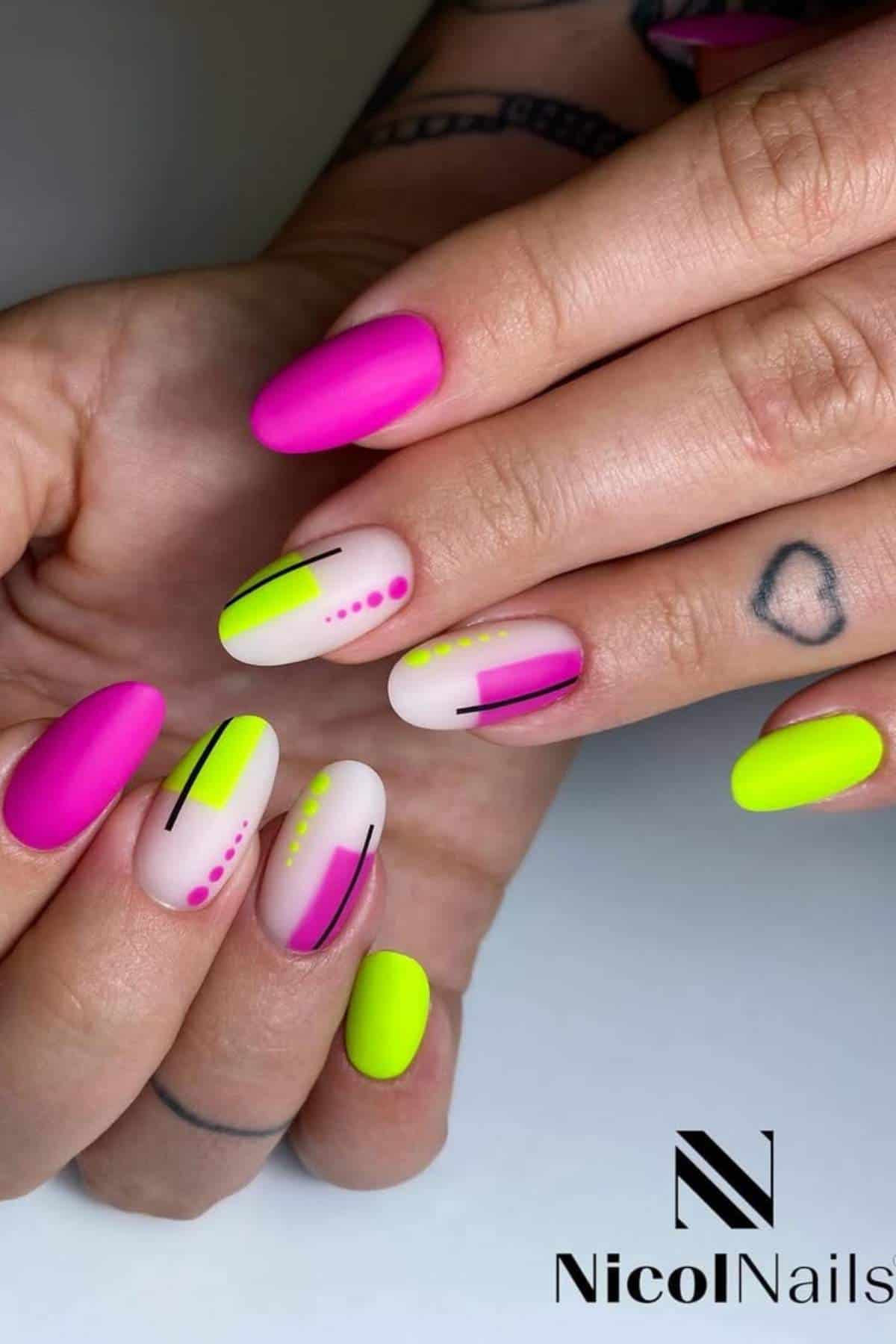 Hands with neon pink and yellow nail polish, featuring black lines and pink dot designs on some nails; tattooed fingers rest beneath.